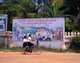 Laos: Two schoolgirls ride their bicycle in front of a Socialist realist-style education and industry poster on the streets of Vientiane